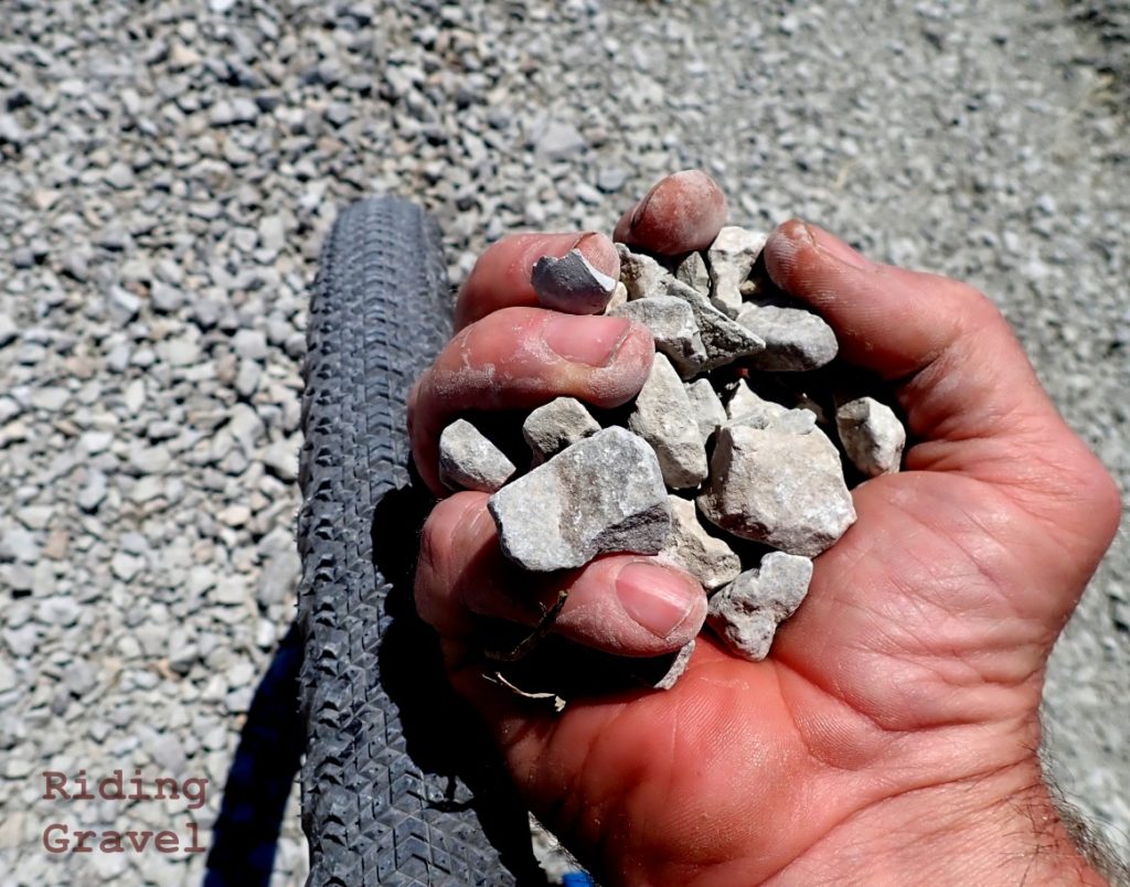 A hand holding crushed rock above a tire on a gravel road.