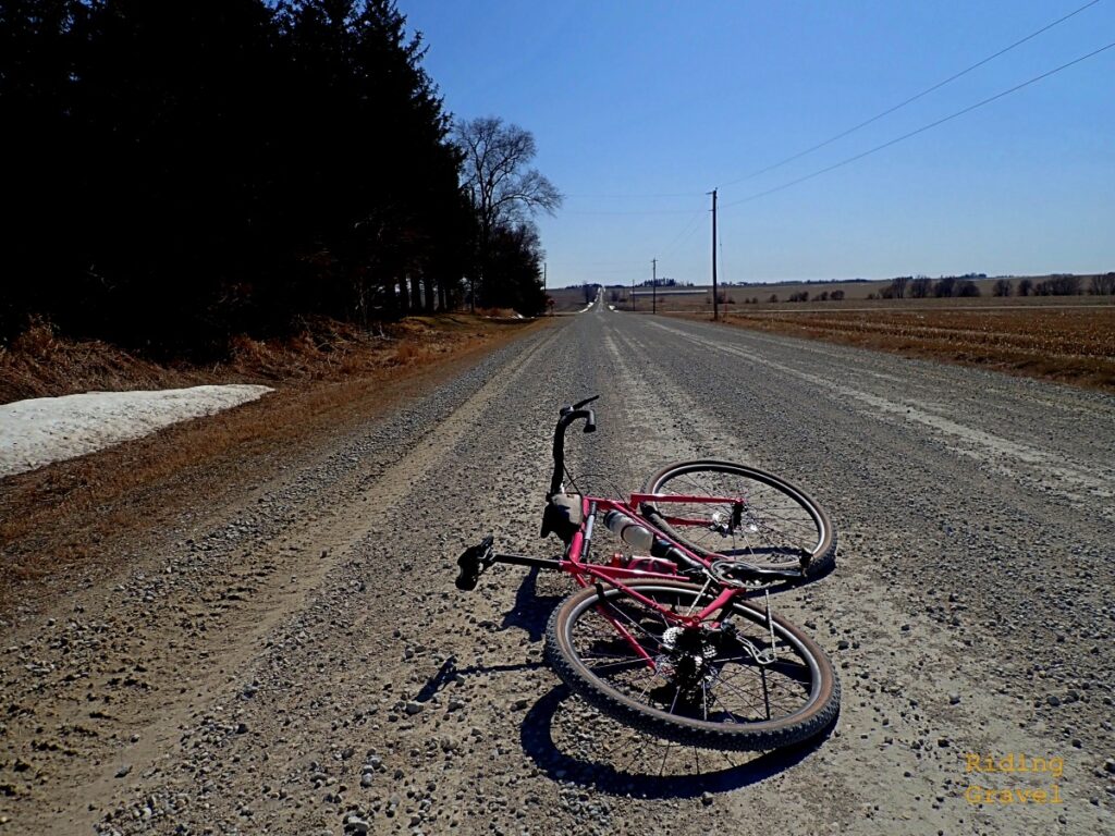 A pink bicycle laying on a crushed rock road