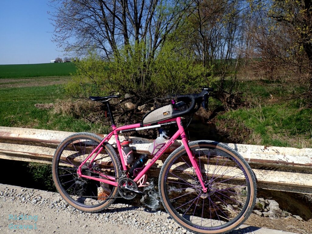 A pink bicycle in a rural setting leaning on a bridge railing.