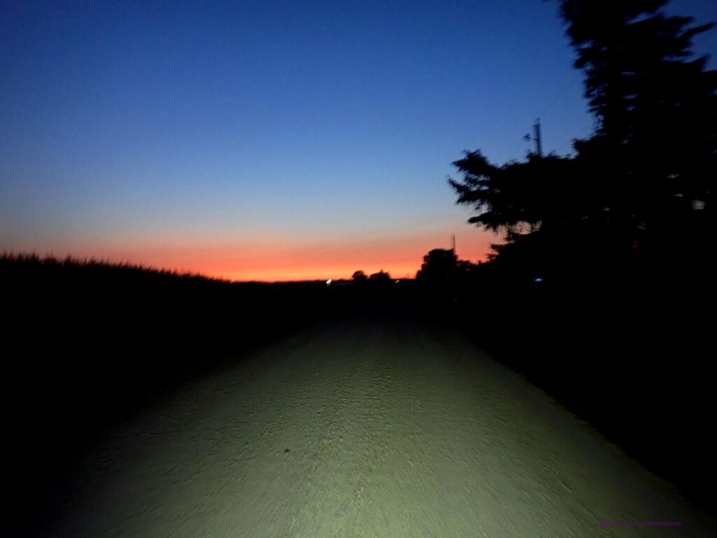 Sunrise on the horizon as a light shines up a rural gravel road.