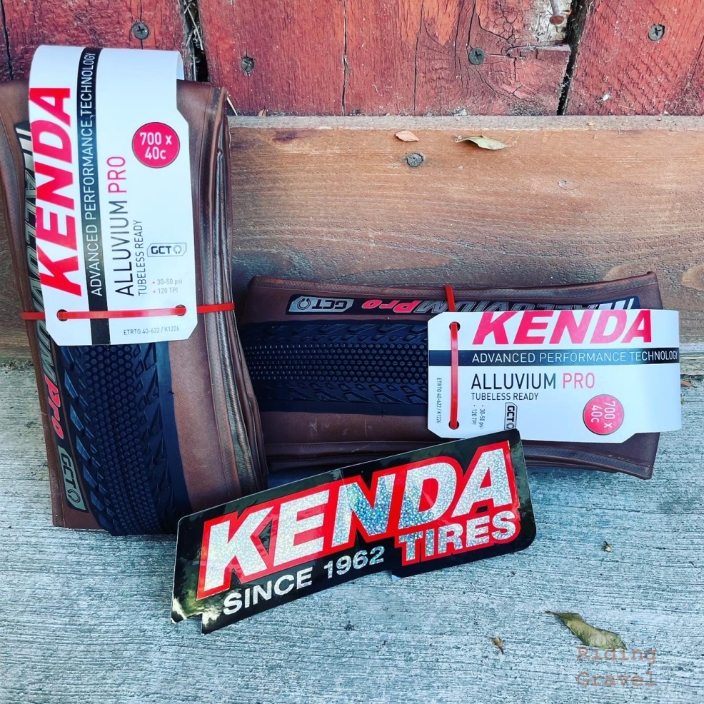 Image showing Kenda Alluvium Pro tires in retail packaging against a wooden wall.