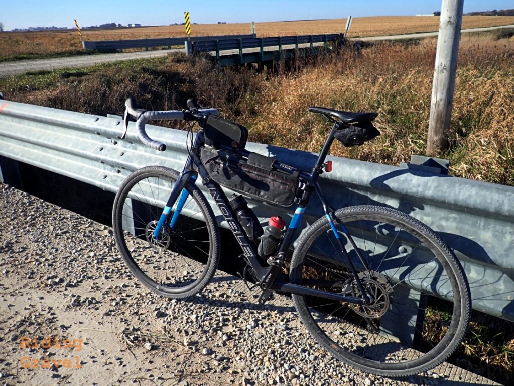 Guitar Ted's gravel bike leaning against a bridge railing in a rural setting.