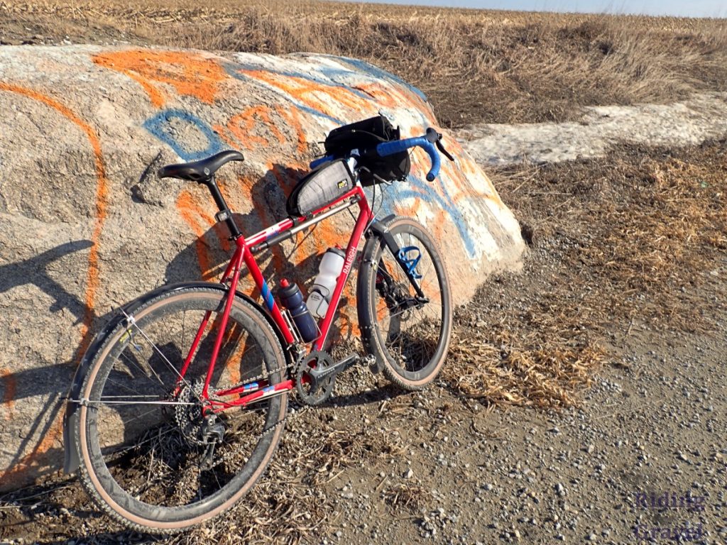 A bicycle lying against a large stone in a rural setting.