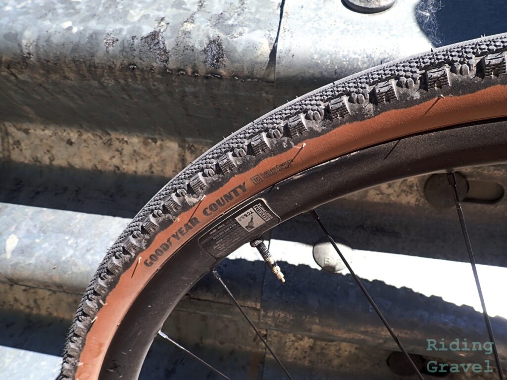 Close-up of the branding on a Goodyear County tire against a railing in a rural setting. 