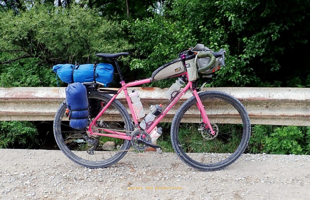 A loaded bike with bags and on a gravel road leaning on a railing. 