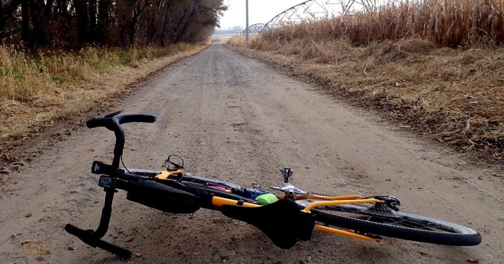 A bicycle laying on a dirt road in a rural area. 