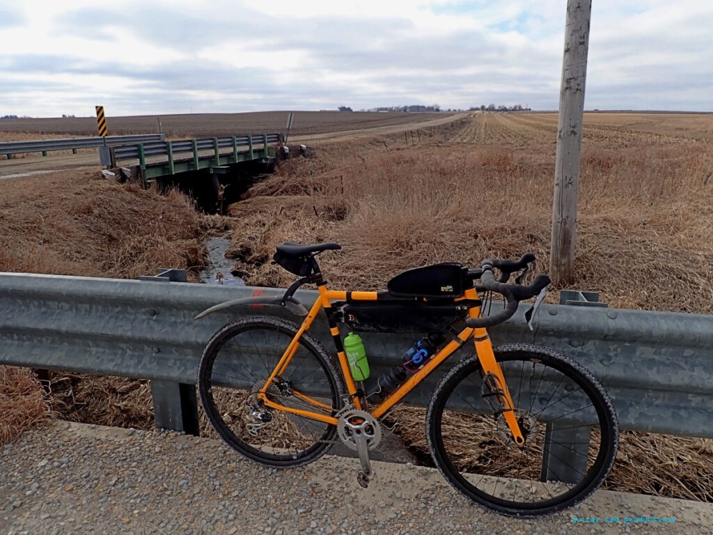 A bicycle on a rural road leaning against a guard rail.