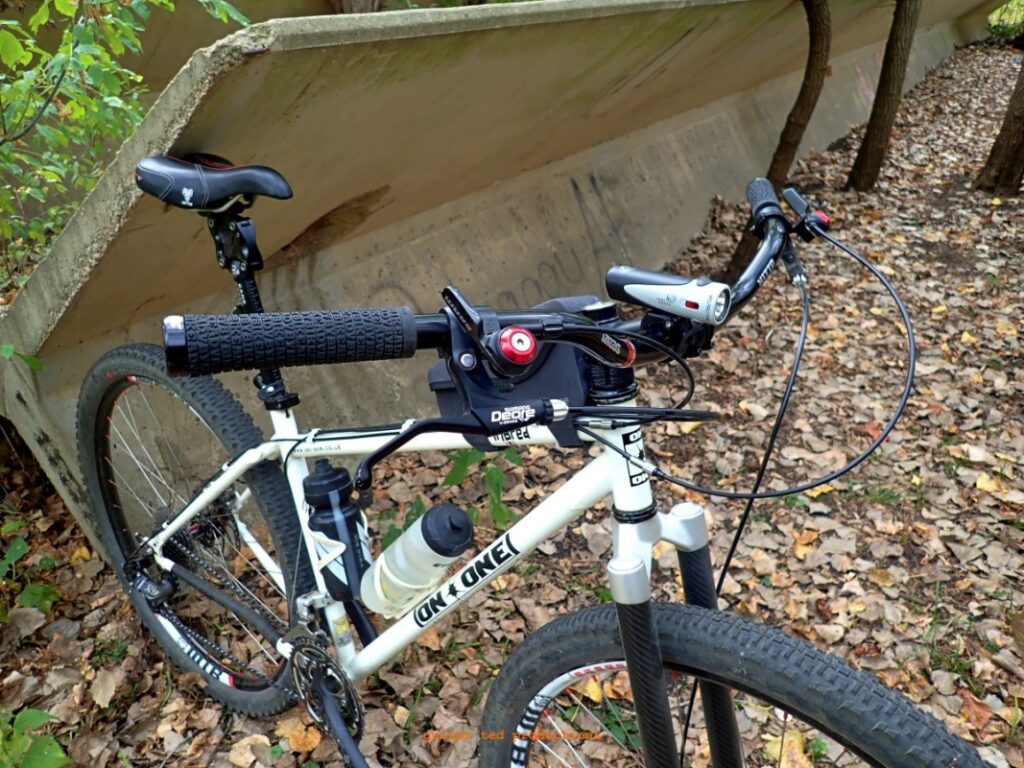 Image of a mountain bike with the X Country Bar leaning against a concrete structure in a wooded setting. 