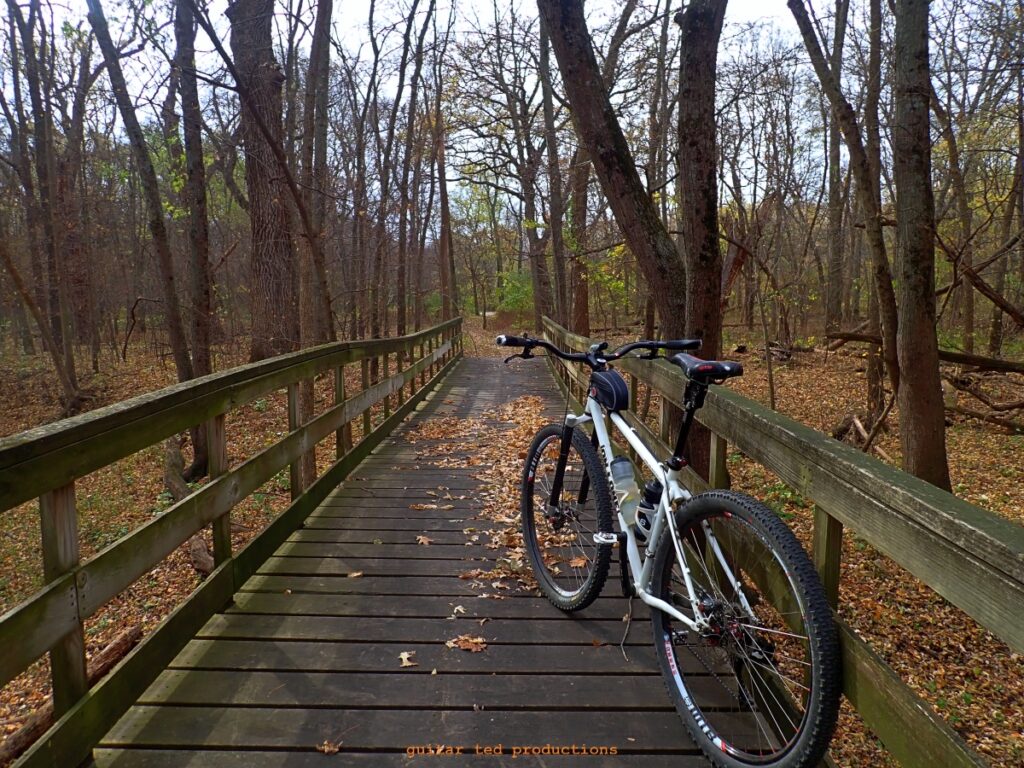 Image of a bicycle with the Wilde Bicycle Co Country Bar on it sitting on a wooden bridge in a wooded setting. 