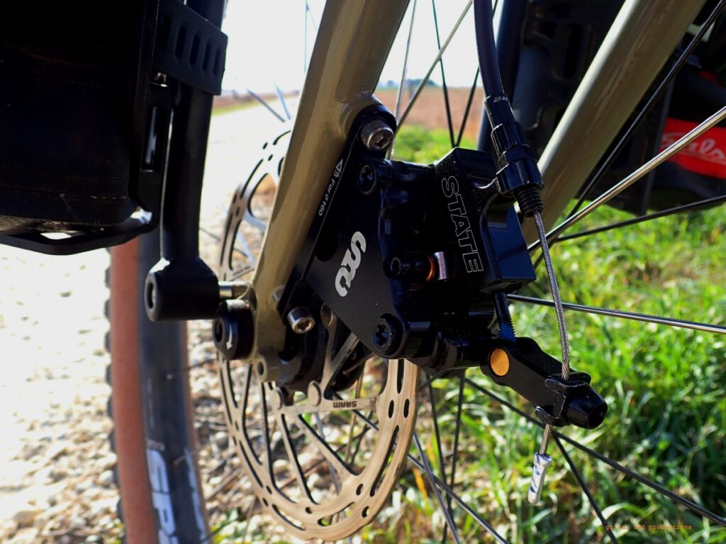 Close-up of a front disc brake caliper on a bicycle in a rural setting. 